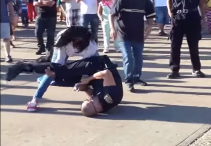 Un flic ceinture blanche tente de mettre un brassard sur une femme ; Elle contre-attaque avec un renversement